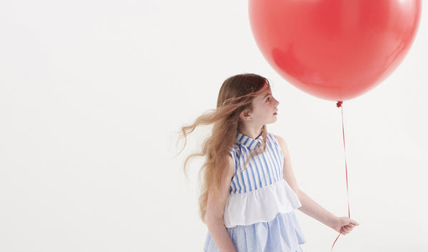 Girl with a red balloon wearing a ruffled dress as an example of trends in children's clothing
